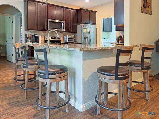 kitchen featuring hardwood / wood-style flooring, light stone countertops, appliances with stainless steel finishes, and a kitchen breakfast bar