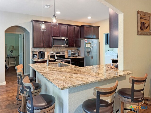 kitchen featuring a breakfast bar, hanging light fixtures, backsplash, stainless steel appliances, and independent washer and dryer