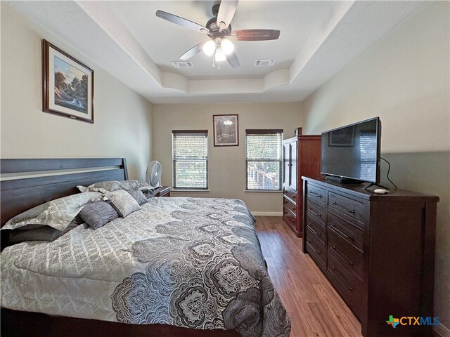 bedroom with hardwood / wood-style flooring, ceiling fan, and a raised ceiling