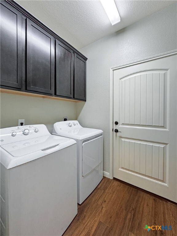 laundry room featuring cabinets, dark hardwood / wood-style flooring, separate washer and dryer, and a textured ceiling