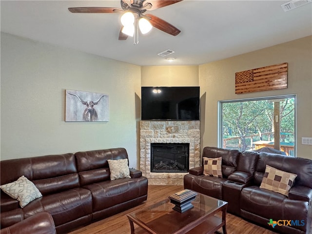 living room featuring ceiling fan, wood-type flooring, and a stone fireplace