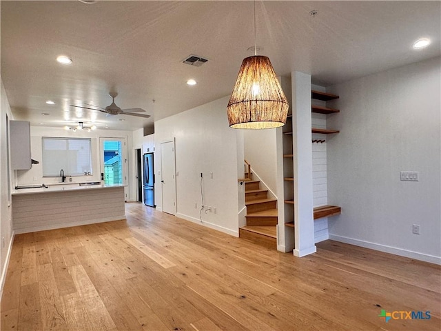 unfurnished living room with light wood-type flooring, ceiling fan, and sink