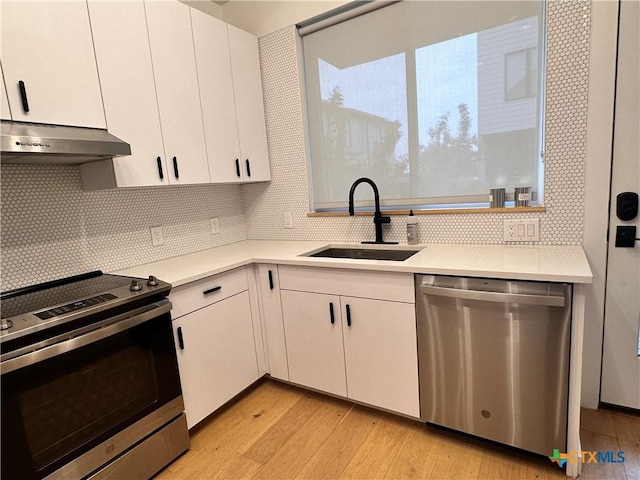 kitchen with decorative backsplash, appliances with stainless steel finishes, sink, white cabinets, and light hardwood / wood-style floors