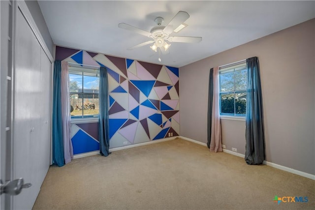 spare room with an accent wall, carpet flooring, baseboards, and ceiling fan