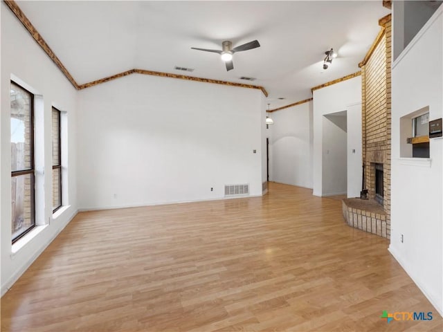 unfurnished living room with ceiling fan, vaulted ceiling, a brick fireplace, light hardwood / wood-style floors, and ornamental molding