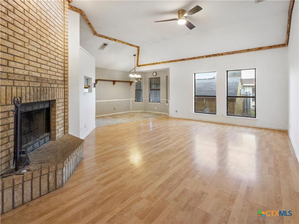 unfurnished living room featuring a brick fireplace, light hardwood / wood-style floors, ceiling fan with notable chandelier, and crown molding