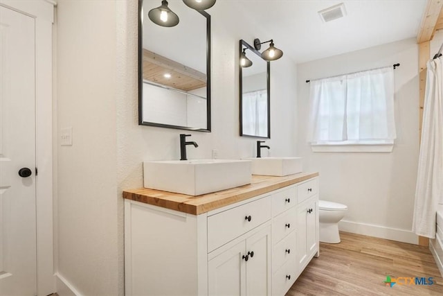 413 S Tyler St, Mcgregor, TX 76657 - bathroom featuring baseboards, double vanity, toilet, wood finished floors, and curtained shower