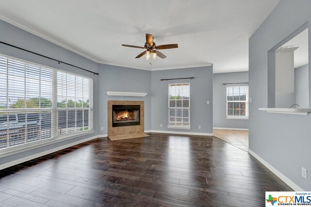 unfurnished living room featuring ornamental molding, a tiled fireplace, dark wood-type flooring, and ceiling fan