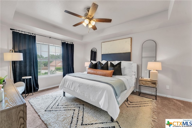 carpeted bedroom featuring ceiling fan and a raised ceiling