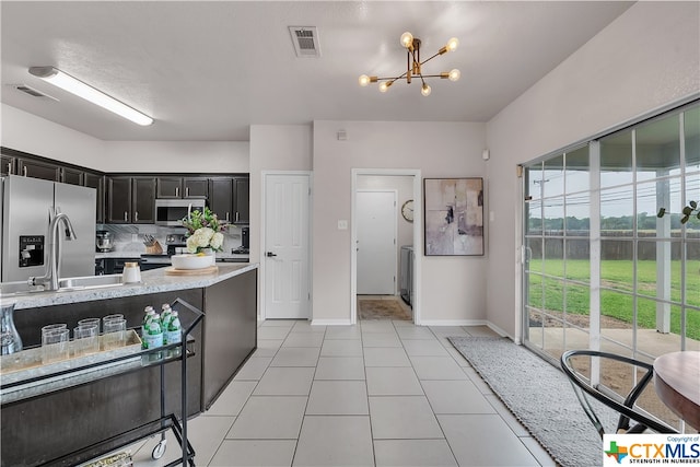 kitchen with stainless steel appliances, a textured ceiling, light tile patterned floors, a notable chandelier, and decorative backsplash