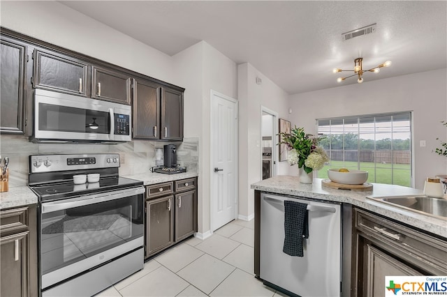 kitchen featuring tasteful backsplash, appliances with stainless steel finishes, dark brown cabinetry, light tile patterned floors, and a notable chandelier