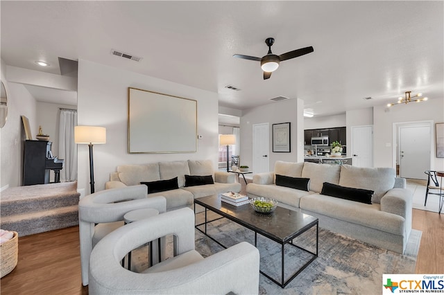 living room with ceiling fan with notable chandelier and wood-type flooring