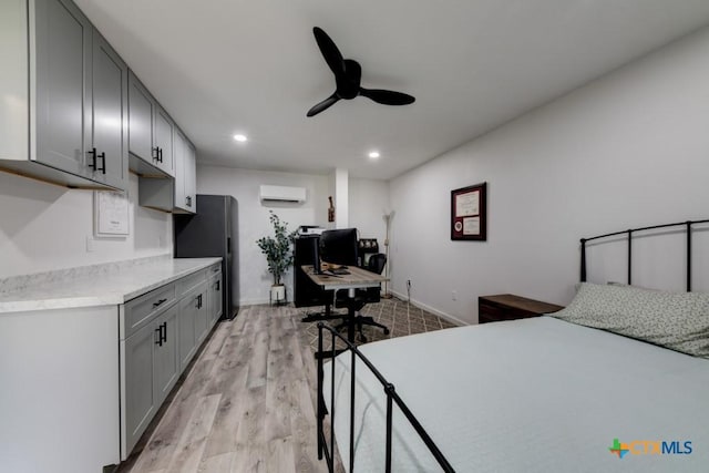 bedroom with a wall unit AC, light hardwood / wood-style floors, ceiling fan, and black fridge