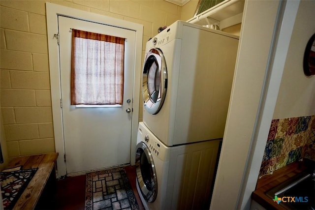 laundry area featuring laundry area, stacked washing maching and dryer, and concrete block wall