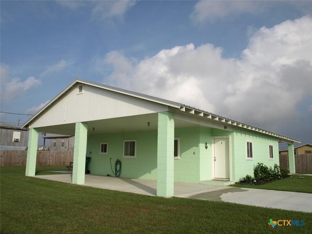 rear view of house featuring an attached carport, fence, concrete block siding, a yard, and a patio area