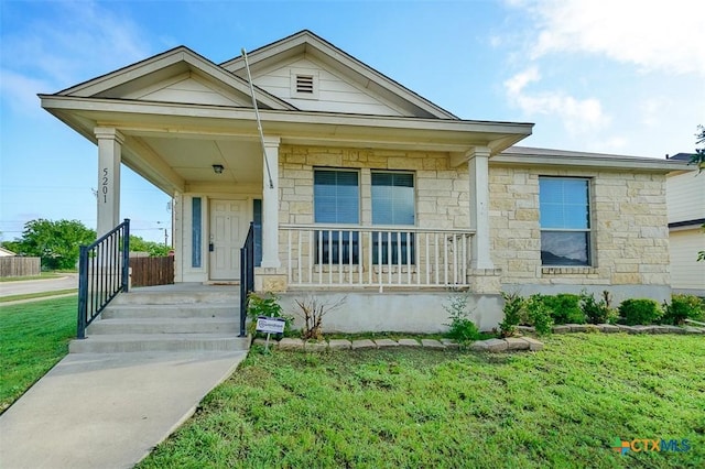 view of front of house with stone siding, a front yard, and covered porch