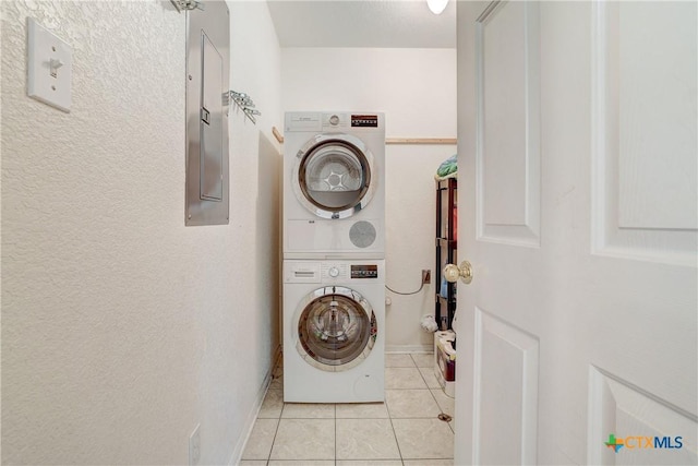 laundry area featuring laundry area, electric panel, stacked washer / drying machine, baseboards, and light tile patterned flooring