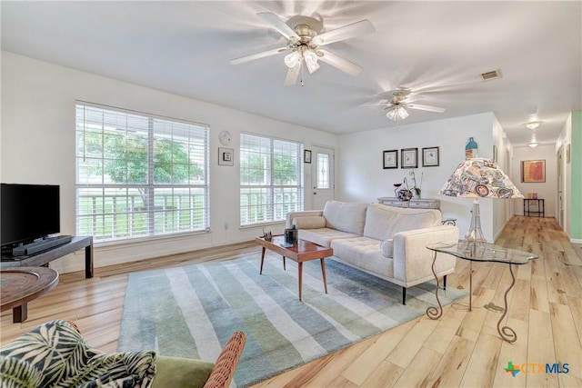 living room featuring light wood-type flooring, a ceiling fan, baseboards, and visible vents