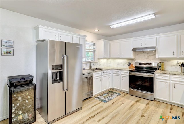 kitchen with under cabinet range hood, stainless steel appliances, white cabinetry, and light wood-style floors