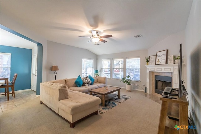 living area featuring a ceiling fan, visible vents, lofted ceiling, a tile fireplace, and light carpet