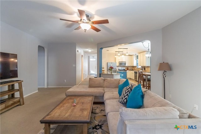 living room featuring light carpet, baseboards, arched walkways, and ceiling fan