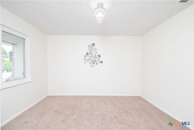 spare room featuring light colored carpet, baseboards, and a textured ceiling