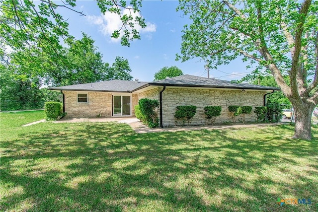 view of front of home with stone siding, a patio area, roof with shingles, and a front yard