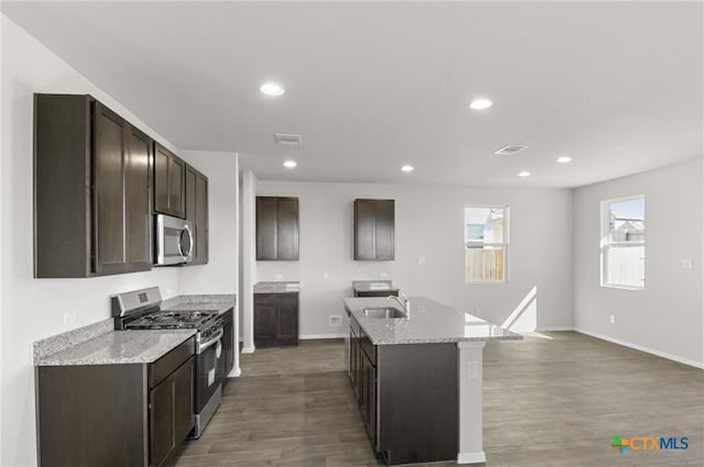 kitchen with sink, an island with sink, dark hardwood / wood-style flooring, light stone counters, and stainless steel appliances