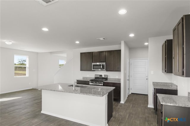 kitchen featuring light stone countertops, sink, dark hardwood / wood-style flooring, a kitchen island with sink, and appliances with stainless steel finishes