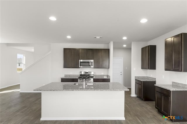 kitchen with dark hardwood / wood-style floors, light stone counters, an island with sink, and appliances with stainless steel finishes