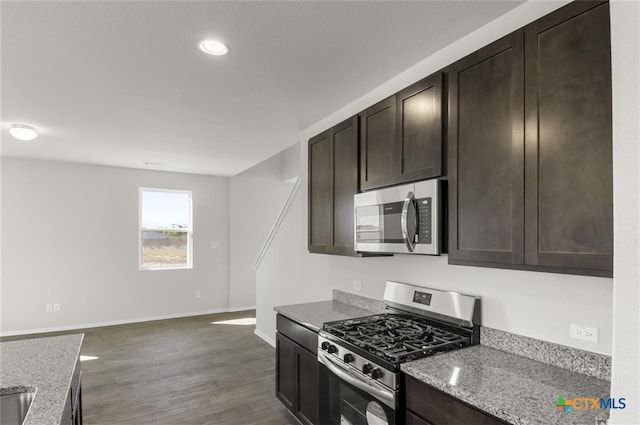 kitchen with light stone countertops, appliances with stainless steel finishes, dark brown cabinetry, and dark wood-type flooring