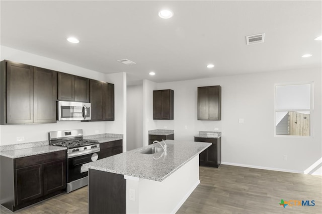 kitchen with light stone countertops, stainless steel appliances, sink, hardwood / wood-style floors, and an island with sink