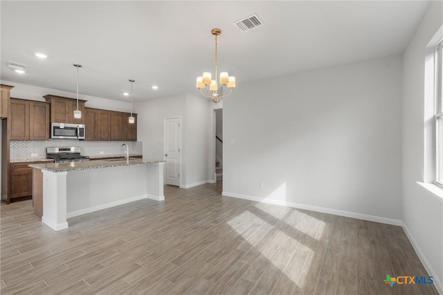 kitchen featuring stainless steel appliances, sink, hanging light fixtures, a kitchen island with sink, and light stone counters