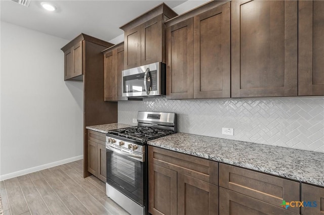 kitchen with appliances with stainless steel finishes, backsplash, light stone counters, light hardwood / wood-style flooring, and dark brown cabinets