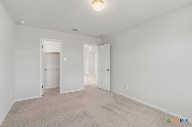 unfurnished bedroom featuring a walk in closet, a closet, and light carpet