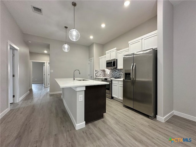 kitchen with appliances with stainless steel finishes, pendant lighting, white cabinetry, sink, and a center island with sink