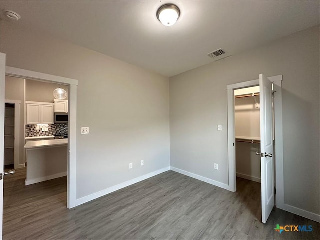 unfurnished bedroom featuring a spacious closet, wood-type flooring, and a closet