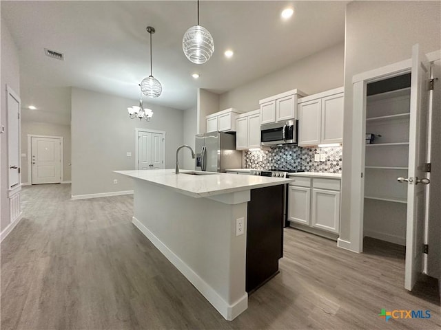 kitchen featuring sink, appliances with stainless steel finishes, pendant lighting, a kitchen island with sink, and white cabinets