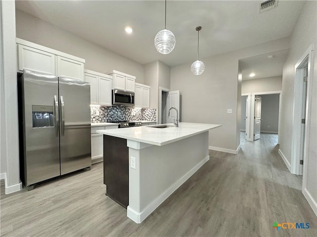 kitchen with pendant lighting, sink, white cabinets, a kitchen island with sink, and stainless steel appliances