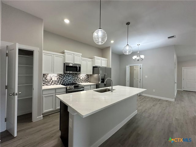 kitchen with hanging light fixtures, an island with sink, white cabinets, and appliances with stainless steel finishes