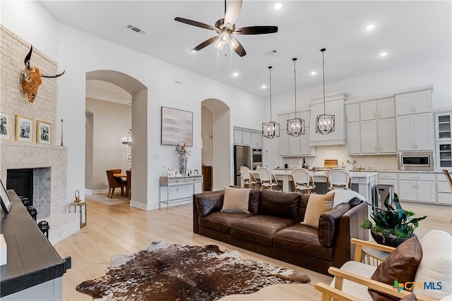 living room with light hardwood / wood-style flooring, a fireplace, ceiling fan, and a high ceiling