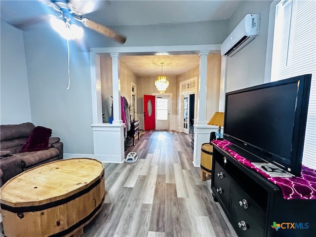 living room with decorative columns, a wall unit AC, wood-type flooring, and ceiling fan with notable chandelier