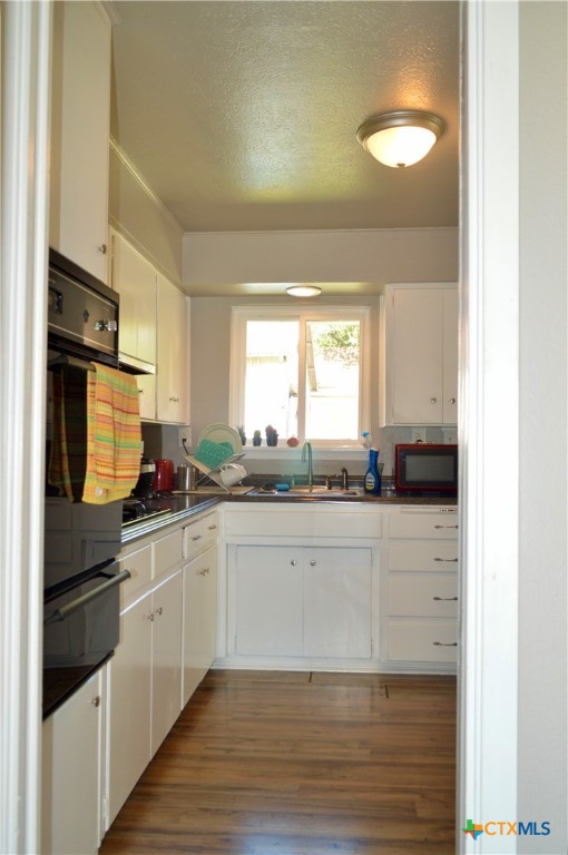 kitchen featuring white cabinetry, sink, black appliances, a textured ceiling, and wood-type flooring