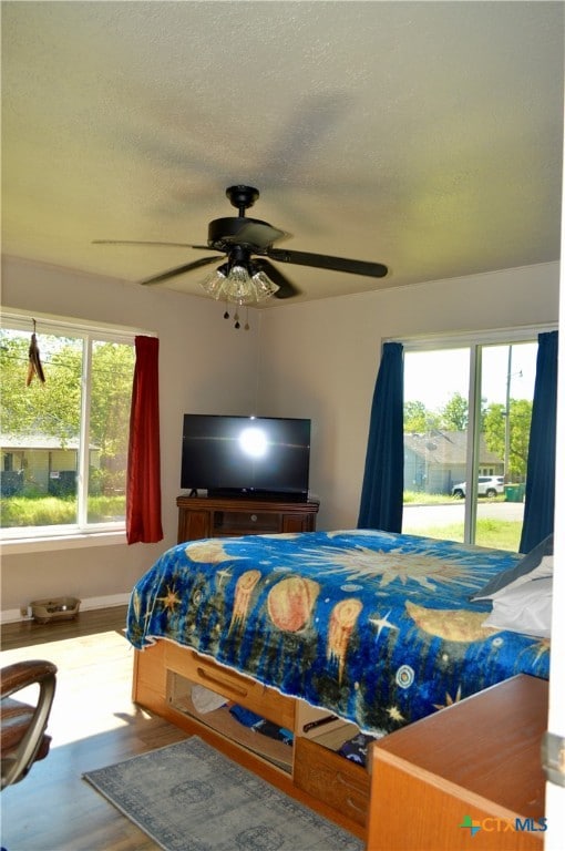 bedroom with hardwood / wood-style floors, ceiling fan, multiple windows, and a textured ceiling