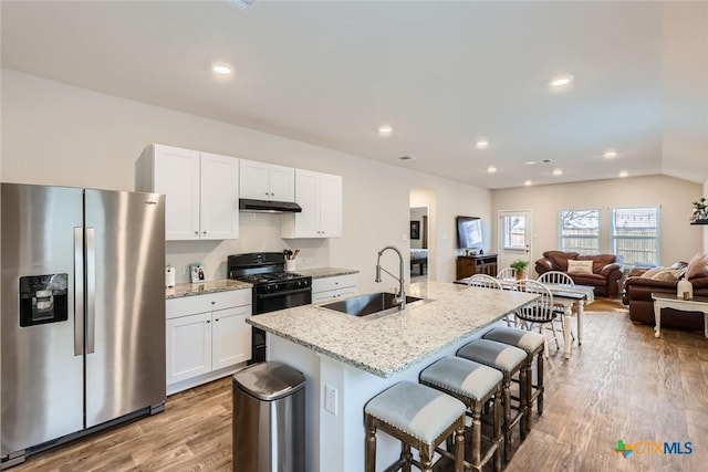 kitchen featuring black range with gas stovetop, a kitchen island with sink, sink, white cabinets, and stainless steel fridge with ice dispenser