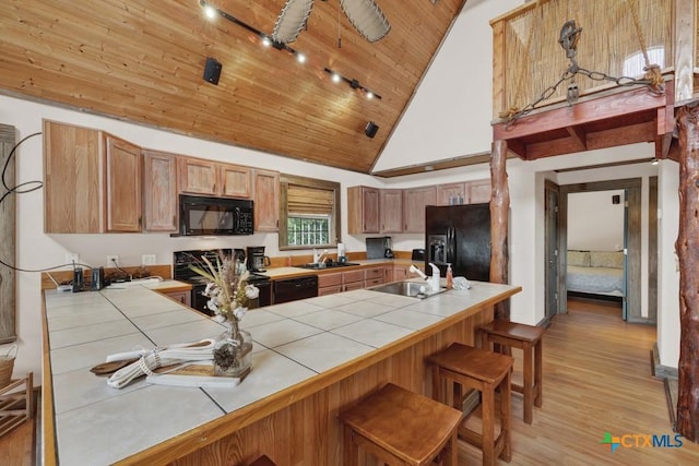 kitchen with tile countertops, sink, a kitchen bar, wood ceiling, and black appliances