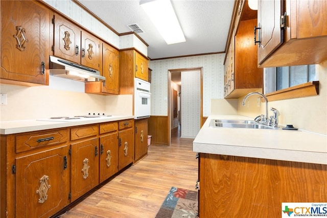 kitchen with sink, light hardwood / wood-style floors, a textured ceiling, white appliances, and ornamental molding