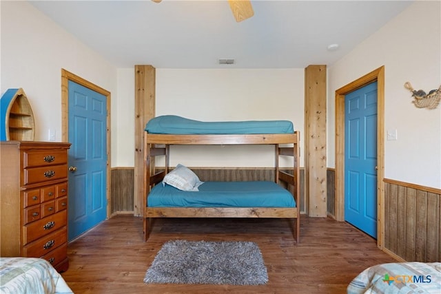 bedroom featuring ceiling fan, dark hardwood / wood-style flooring, and wood walls