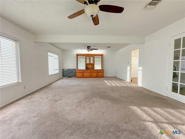 unfurnished living room with a textured ceiling, a ceiling fan, visible vents, and light colored carpet