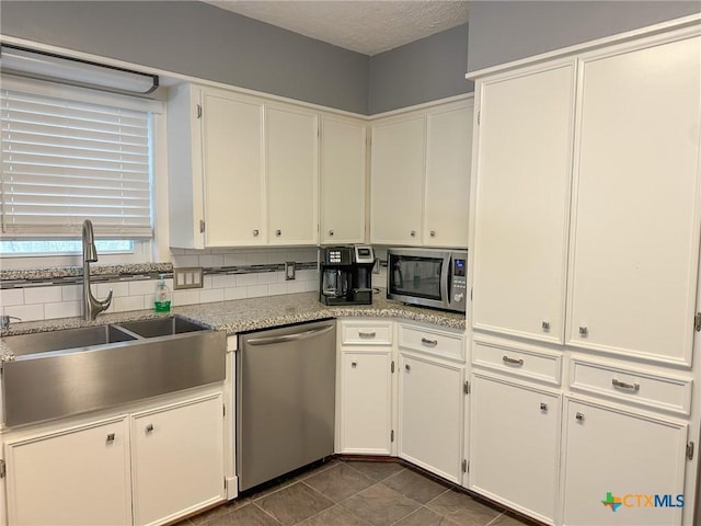 kitchen with tasteful backsplash, appliances with stainless steel finishes, light stone countertops, white cabinetry, and a sink